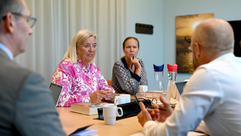 Två kvinnor sitter och lyssnar och pratar i ett mötesrum med andra människor.